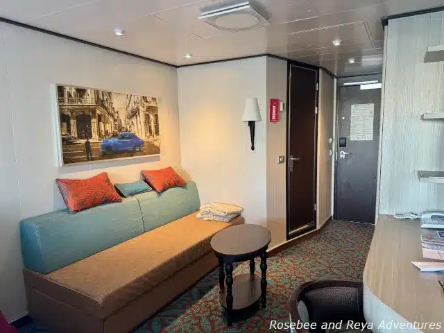 Picture of the inside of a Havana stateroom, looking towards the couch, desk, and doors to the bathroom and exit of the room.